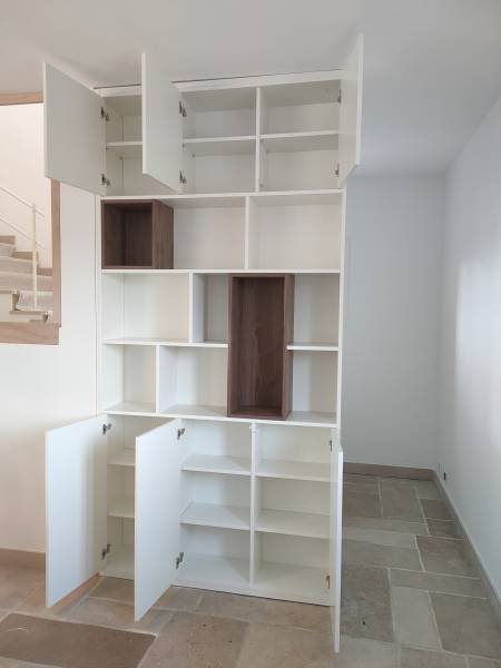 Rangements dissimulés par des portes battantes en mélaminé blanc dans une bibliothèque avec des niches décoratives